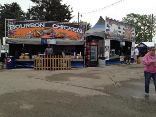 Food vendors at an outdoor fair, featuring a Bourbon Chicken stand and various other food options.