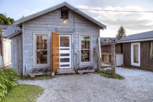 A quaint wooden candy store with an open door, surrounded by gravel and greenery, under a cloudy sky.