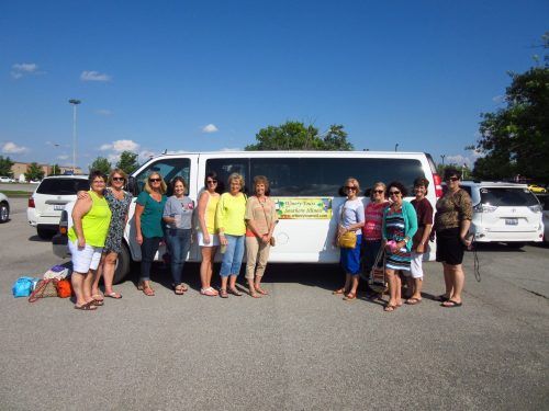 A group of women stands in front of a white van, smiling and posing for a photo on a sunny day.
