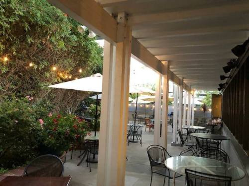 Outdoor dining area with tables, chairs, and umbrellas, surrounded by greenery and string lights.