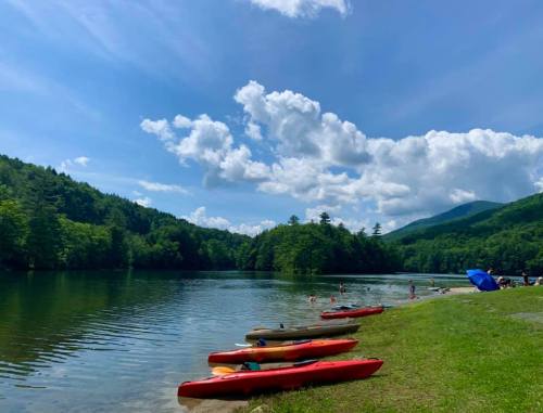 A serene lake surrounded by green trees, with colorful kayaks on the shore and people enjoying the water under a blue sky.