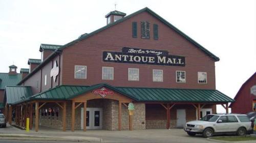 Exterior of a large, rustic antique mall with a green roof and wooden siding, featuring a sign that reads "Antique Mall."