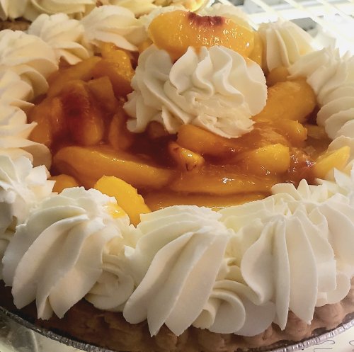 A close-up of a peach pie topped with whipped cream and glazed peach slices.
