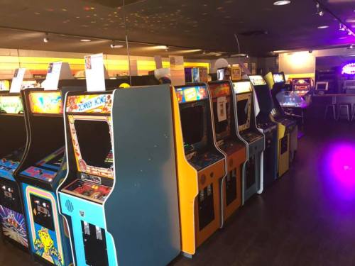 A row of colorful vintage arcade machines in a dimly lit game room.
