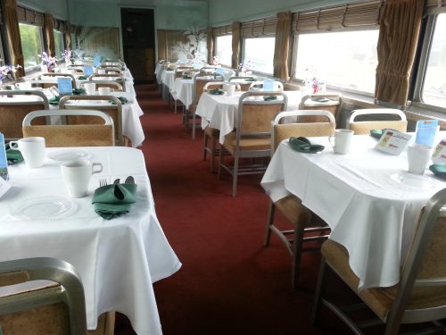 Interior of a dining car with neatly set tables, white tablecloths, and a cozy atmosphere.