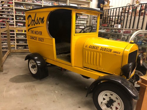 A vintage yellow delivery truck with "Dobson" and "The Mover Since 1927" painted on the side, displayed indoors.