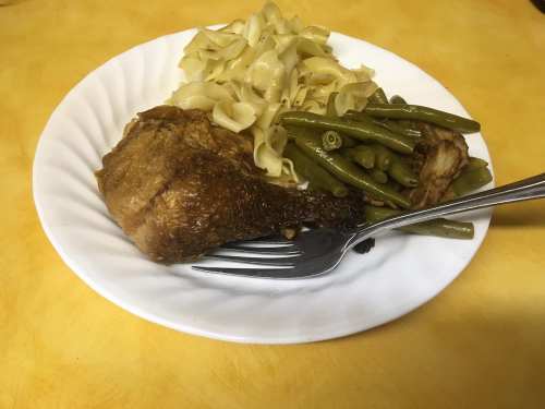 A plate of food featuring a fried chicken leg, green beans, and egg noodles on a yellow background.