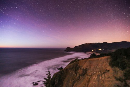 A serene coastal view at dusk, with stars twinkling above and gentle waves lapping against the shore.