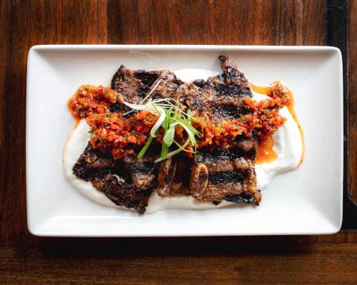 Grilled steak slices topped with a vibrant salsa, served on a creamy white sauce, on a rectangular plate.