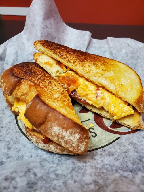 A toasted sandwich filled with melted cheese and a savory egg mixture, served on parchment paper.