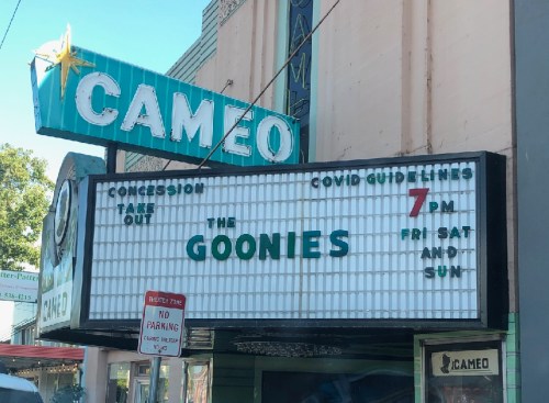 Cameo theater marquee announcing "The Goonies" showing at 7 PM on Friday, Saturday, and Sunday, with COVID guidelines noted.