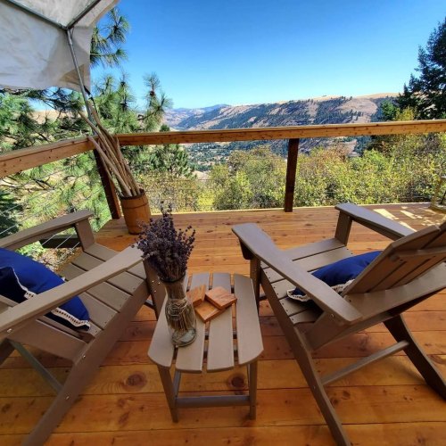 A cozy deck with two chairs, a small table, and a view of mountains and valleys under a clear blue sky.