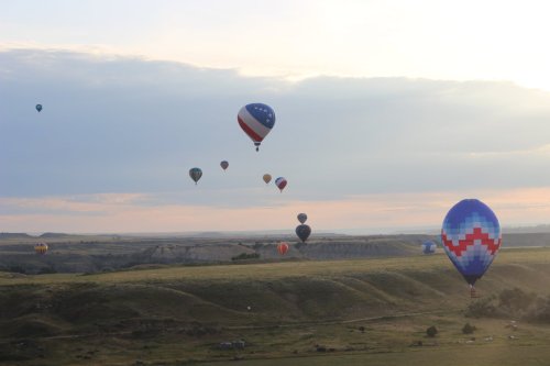 A colorful array of hot air balloons floating over a scenic landscape at sunrise.