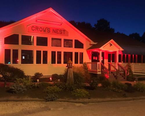 A restaurant named "Crow's Nest" illuminated in red light at night, featuring large windows and a welcoming entrance.