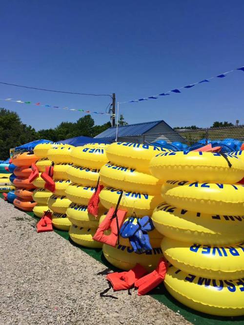 A stack of yellow inflatable tubes and life jackets against a clear blue sky, with colorful flags in the background.