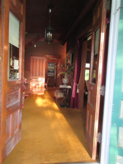 A warmly lit entrance with wooden doors, leading to a cozy interior featuring a table and decorative plants.