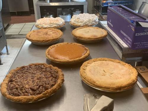 A variety of freshly baked pies on a kitchen counter, including pecan, pumpkin, and coconut cream pies.