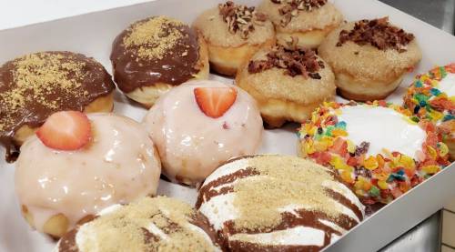 A box of assorted donuts, including chocolate, strawberry, and fruity cereal toppings, with a variety of flavors and textures.