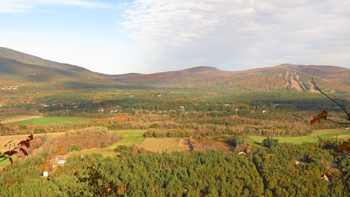 A panoramic view of rolling hills and valleys, showcasing vibrant autumn foliage under a partly cloudy sky.