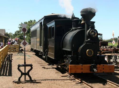 A vintage steam locomotive with a black exterior, parked on tracks at a train station, with people in the background.