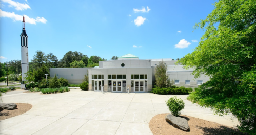 Modern building with a rocket sculpture nearby, surrounded by greenery and under a clear blue sky.