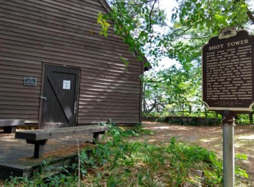 Historic shot tower building with a sign, surrounded by trees and greenery, featuring a wooden bench in the foreground.