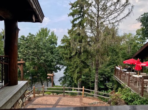 Scenic view of a lake surrounded by trees, with a wooden deck and outdoor dining area in the foreground.