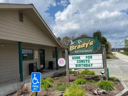 Sign outside Brady's Restaurant reads "Honk for Corey's Birthday," with a parking sign and a cloudy sky in the background.
