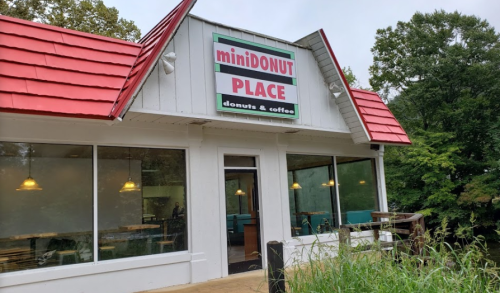 Exterior of miniDONUT Place, a donut and coffee shop with a red roof and large windows, surrounded by greenery.