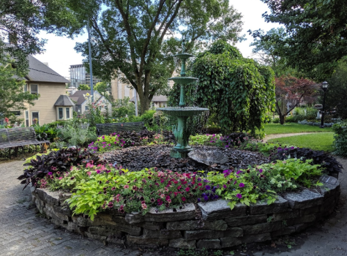 A decorative fountain surrounded by colorful flowers and lush greenery in a serene park setting.