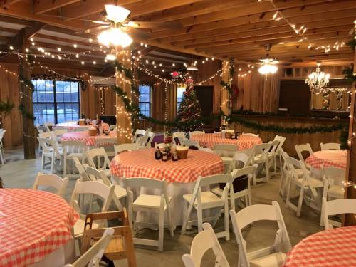 A cozy event space with round tables, checkered tablecloths, string lights, and a decorated Christmas tree.