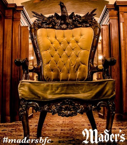 An ornate, vintage chair with a tufted yellow seat and a decorative eagle crest on the back, set in a wooden interior.
