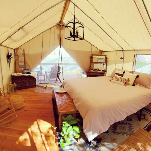 Cozy glamping tent interior with a bed, wooden furniture, and a view of nature through an open entrance.