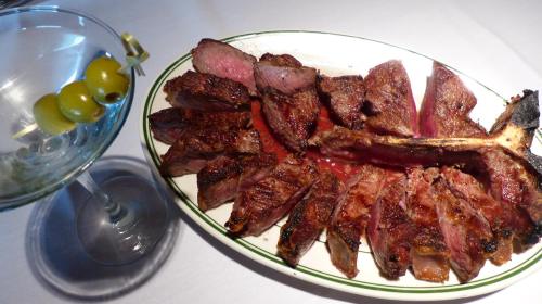 A platter of sliced steak with a martini glass featuring olives on the side.