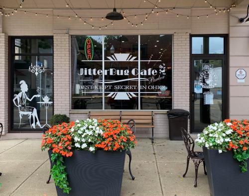 Exterior of JitterBug Cafe with a sign reading "Best Kept Secret in Ohio," surrounded by colorful flower pots.