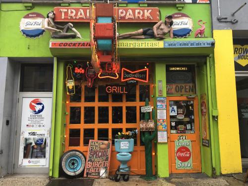 Colorful storefront with neon signs, vintage decor, and a welcoming "Open" sign, featuring a grill and sandwich offerings.
