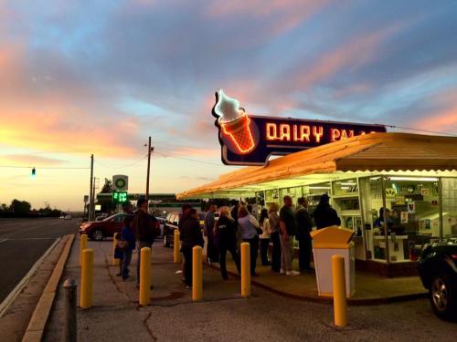 A colorful sunset over a busy ice cream shop with a neon sign, as customers line up outside.