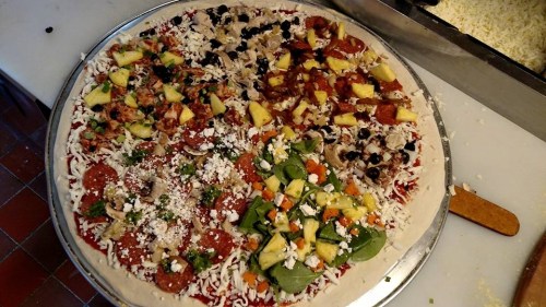 A large pizza divided into sections with various toppings, including pepperoni, vegetables, and pineapple.