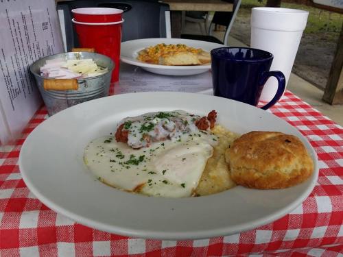 A plate of chicken and biscuits with gravy, served with a side of grits, on a checkered tablecloth.