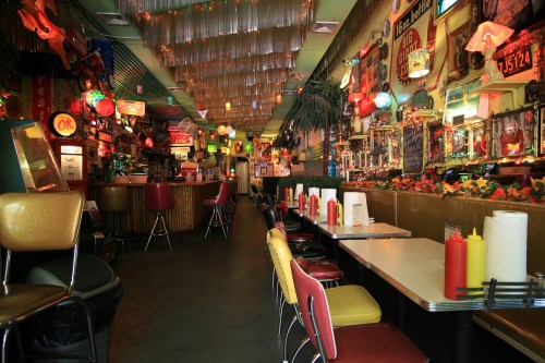 Colorful diner interior with retro decor, neon lights, and tables set with condiments. A vibrant, lively atmosphere.