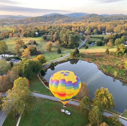 A colorful hot air balloon floats above a serene pond, surrounded by autumn foliage and rolling hills.
