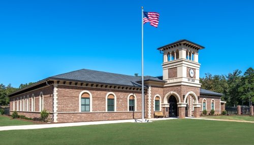 A brick building with a clock tower, American flag, and green lawn under a clear blue sky.