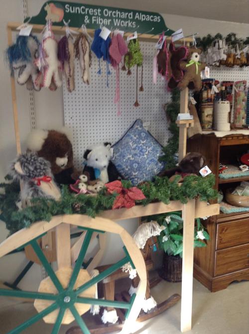 A display cart featuring plush alpacas, colorful yarns, and handmade crafts, decorated with greenery.