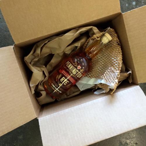 A bottle of whiskey in a cardboard box, surrounded by crumpled paper and protective netting.