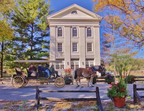 A horse-drawn carriage in front of a historic building, surrounded by colorful autumn foliage and flower planters.