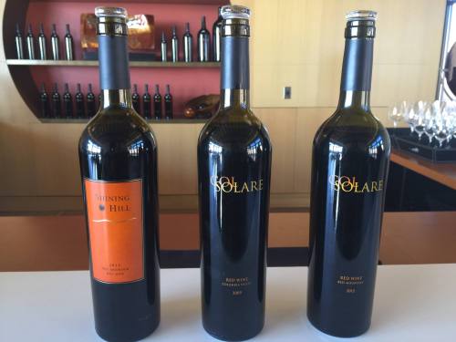 Three wine bottles on a table: "Shining Hill" 2013, "Solare" 2009, and "Solare" 2012, with a winery backdrop.