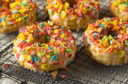 Colorful donuts topped with icing and vibrant cereal pieces, arranged on a cooling rack.