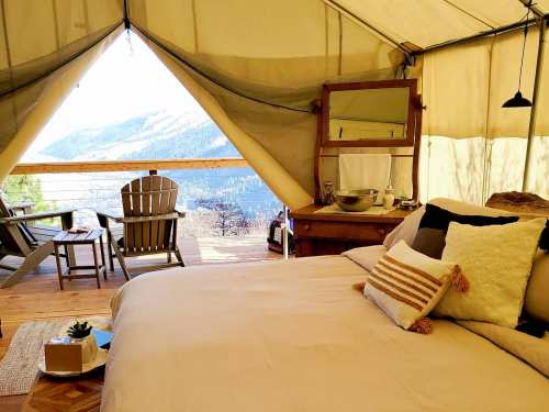 Cozy glamping tent interior with a bed, wooden furniture, and a view of mountains through an open entrance.