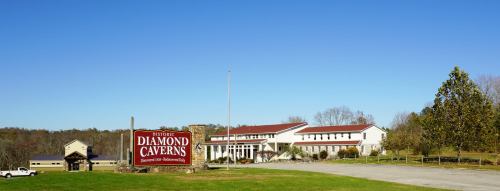 Sign for Historic Diamond Caverns with a building and clear blue sky in the background. Green grass in the foreground.