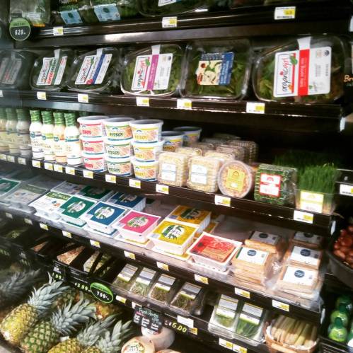 A grocery shelf displaying various packaged foods, including salads, dips, and fresh produce like pineapples.